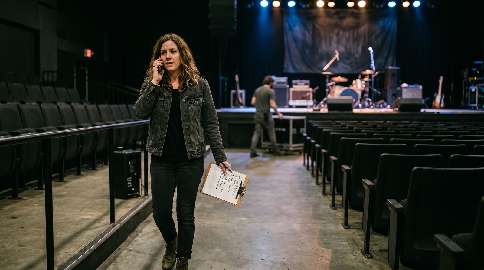 A performer on the phone with a checklist, walking through an empty venue as the stage is set